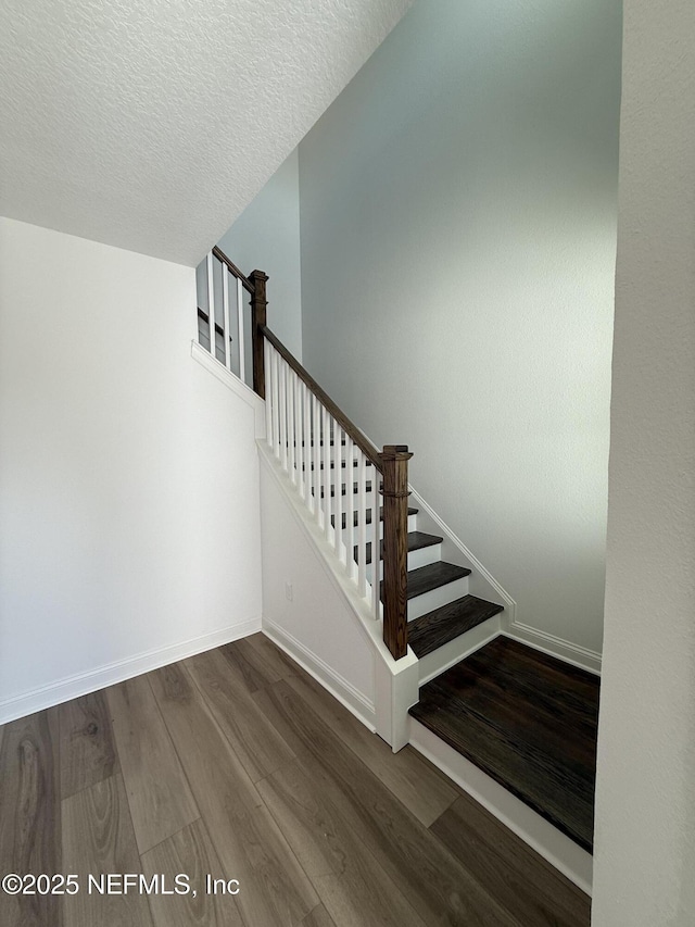 staircase featuring a textured ceiling, baseboards, and wood finished floors