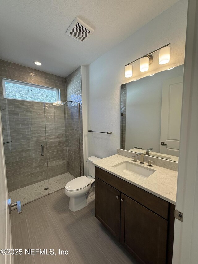 full bath featuring toilet, a stall shower, vanity, and visible vents