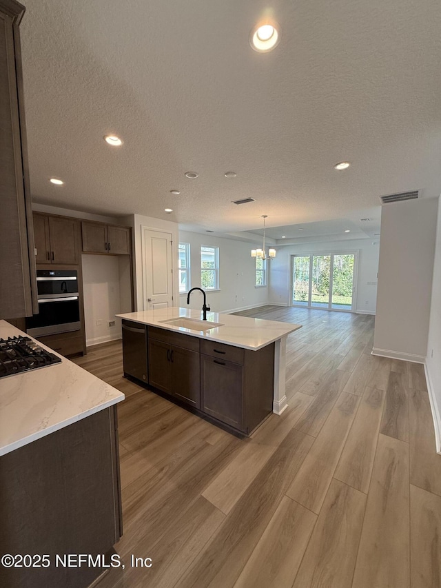 kitchen featuring a kitchen island with sink, a sink, visible vents, open floor plan, and black appliances