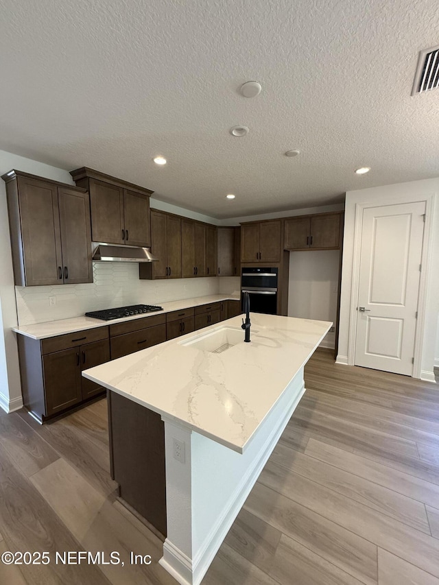 kitchen with a kitchen island with sink, under cabinet range hood, a sink, visible vents, and stainless steel gas stovetop