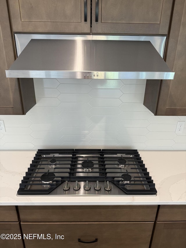 interior details featuring light stone counters, backsplash, wall chimney range hood, and gas stovetop