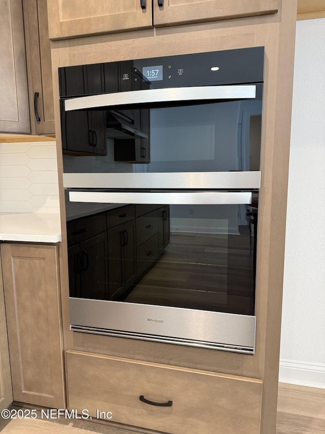 interior details featuring light wood finished floors, tasteful backsplash, light countertops, dobule oven black, and baseboards