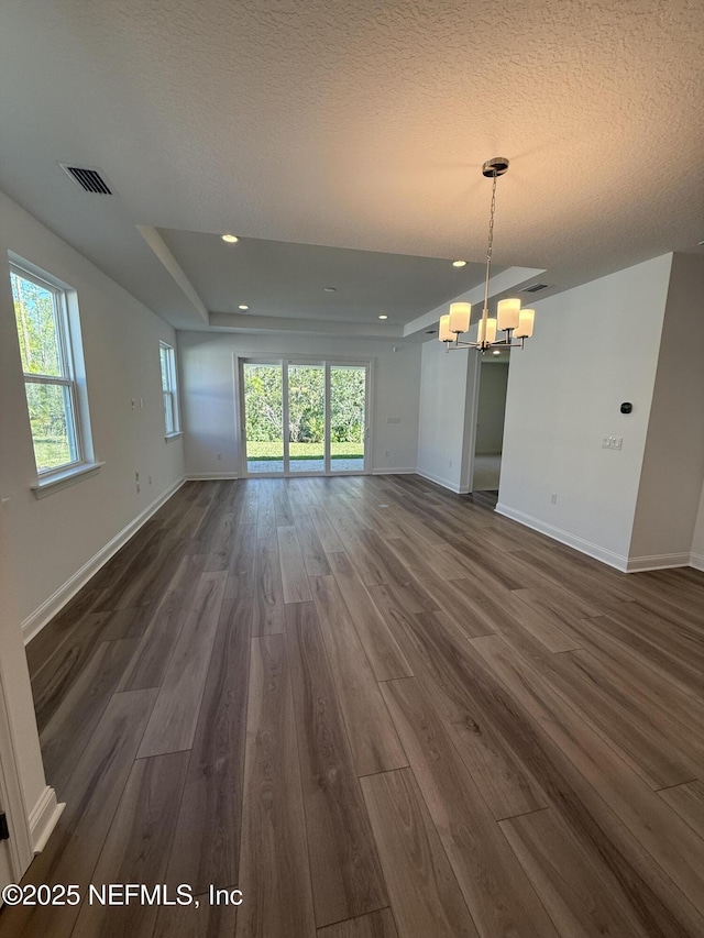 unfurnished living room featuring a notable chandelier, dark wood-type flooring, visible vents, baseboards, and a raised ceiling