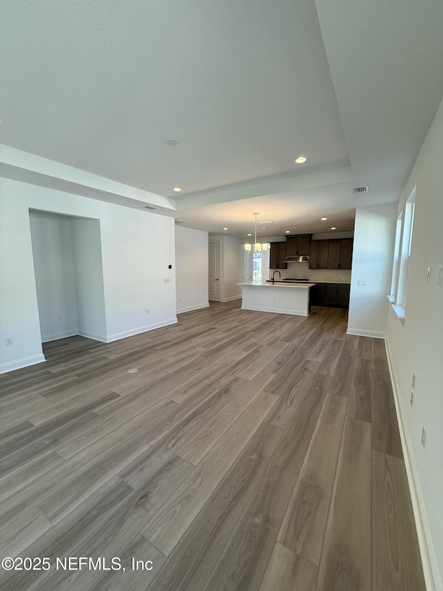 unfurnished living room with recessed lighting, a sink, light wood-style flooring, and baseboards