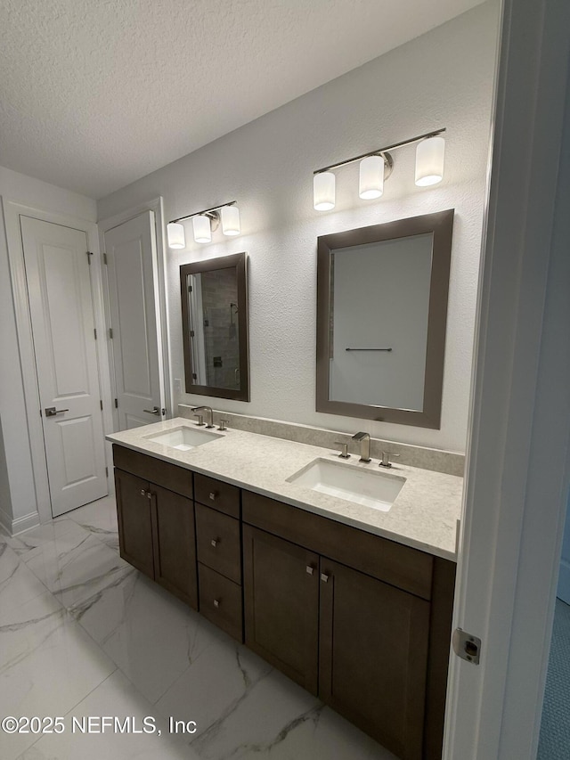 full bathroom with a textured ceiling, marble finish floor, double vanity, and a sink