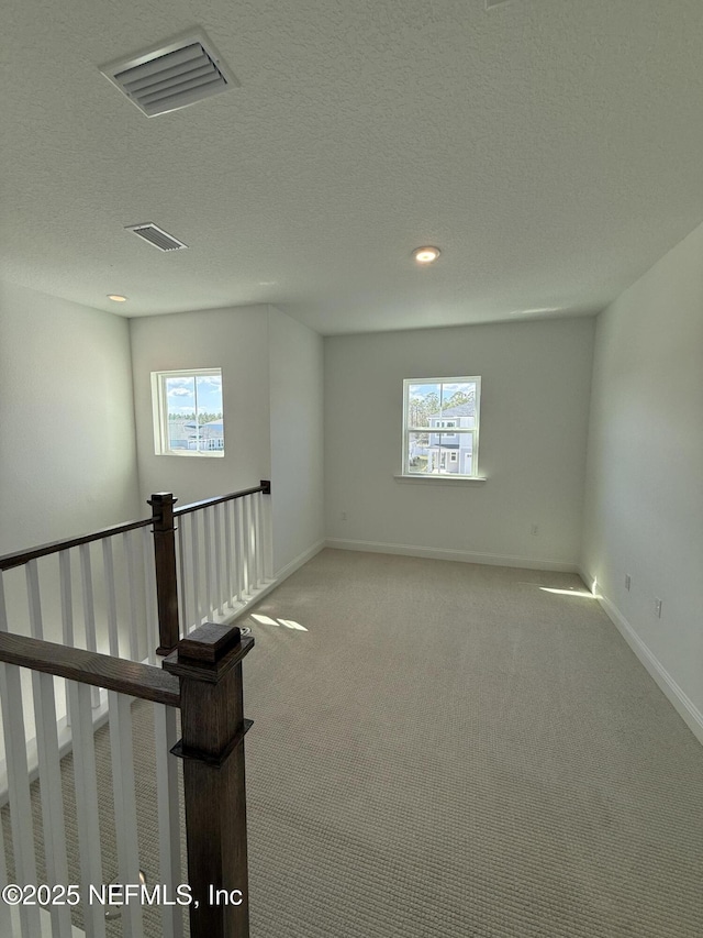 spare room with a healthy amount of sunlight, visible vents, and light colored carpet