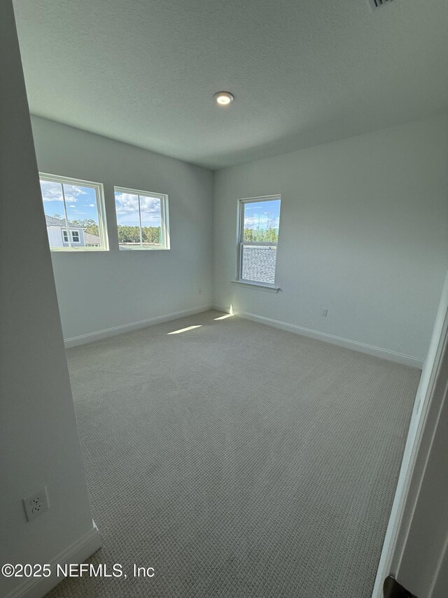 empty room with light colored carpet, a textured ceiling, and baseboards