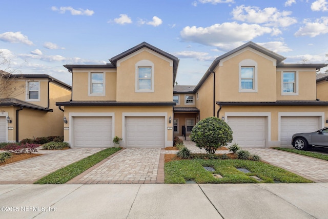 view of property with an attached garage, decorative driveway, and stucco siding