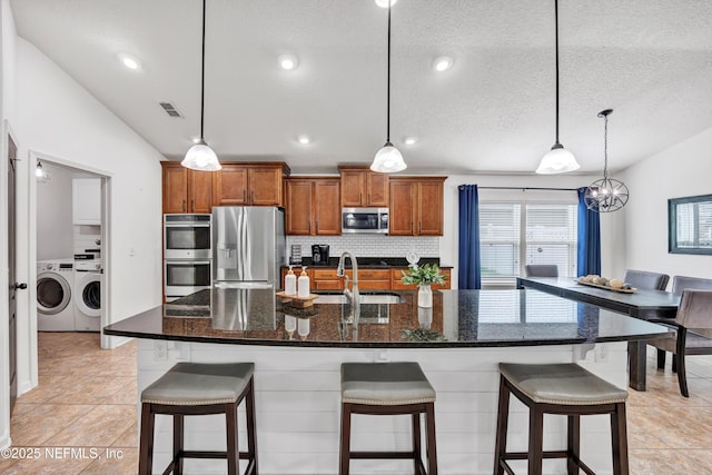 kitchen with sink, stainless steel appliances, hanging light fixtures, and a large island with sink