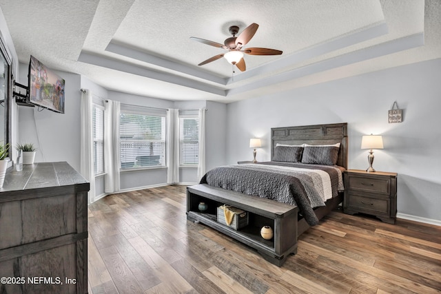 bedroom with ceiling fan, a tray ceiling, dark hardwood / wood-style flooring, and a textured ceiling