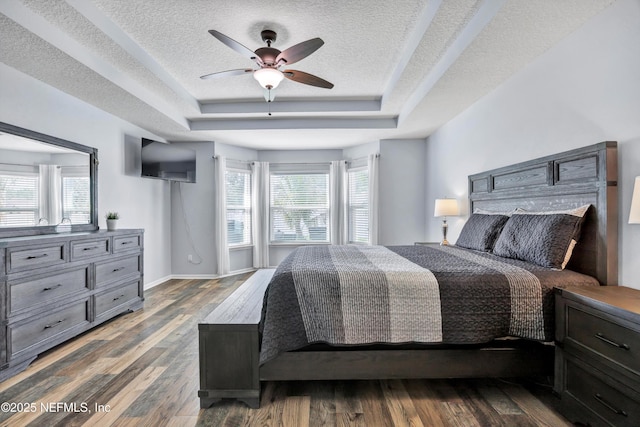 bedroom featuring a tray ceiling, hardwood / wood-style floors, multiple windows, and a textured ceiling