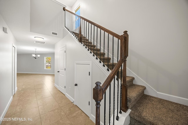 stairway with visible vents, a towering ceiling, an inviting chandelier, baseboards, and tile patterned floors