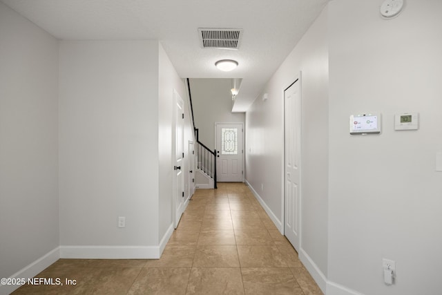 hallway featuring a textured ceiling, light tile patterned floors, visible vents, baseboards, and stairs