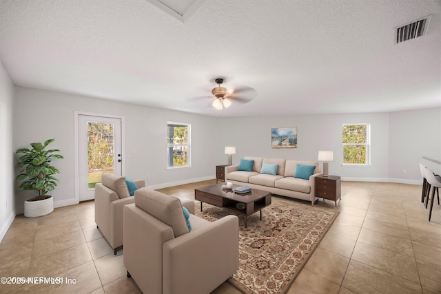 living room featuring a textured ceiling, light tile patterned floors, visible vents, and baseboards