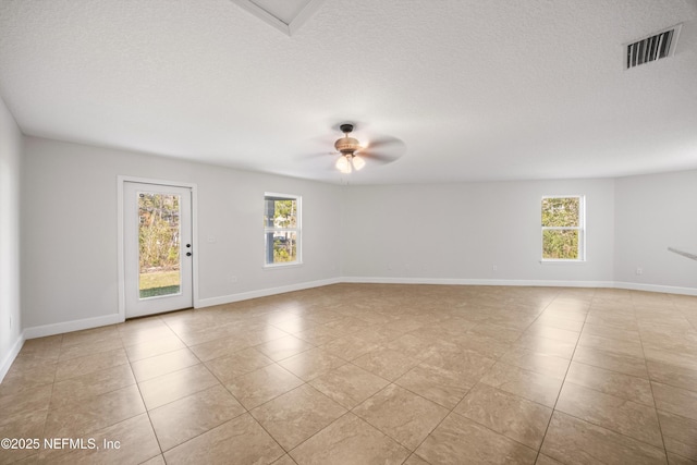 empty room with ceiling fan, a textured ceiling, visible vents, and a wealth of natural light