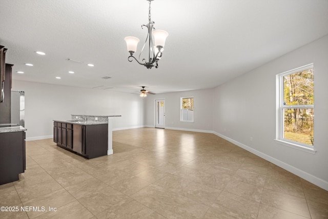 kitchen with dark brown cabinetry, ceiling fan with notable chandelier, a sink, baseboards, and hanging light fixtures