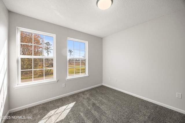 spare room featuring baseboards, dark carpet, and a textured ceiling