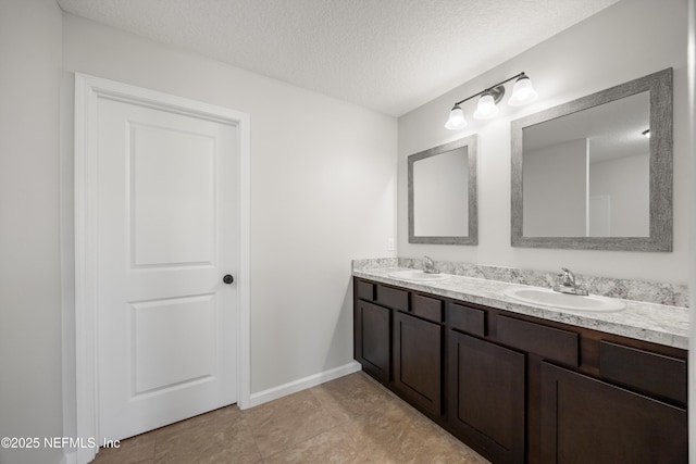 bathroom featuring double vanity, a textured ceiling, baseboards, and a sink