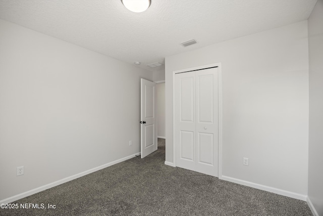 unfurnished bedroom with a closet, visible vents, dark carpet, a textured ceiling, and baseboards