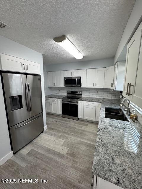 kitchen featuring sink, white cabinetry, stainless steel appliances, tasteful backsplash, and light wood-type flooring