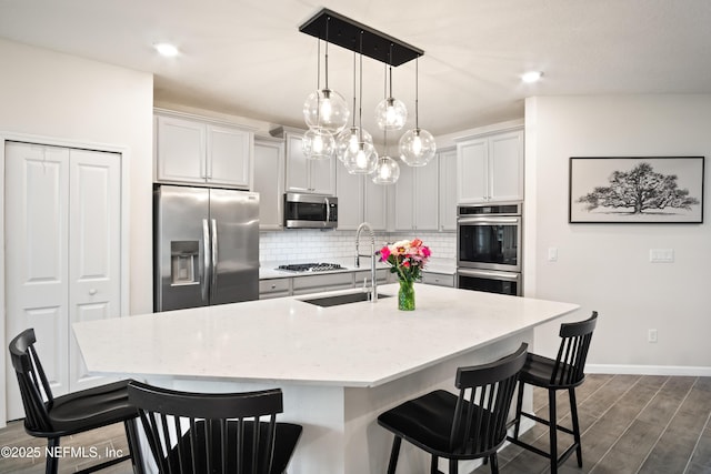 kitchen featuring appliances with stainless steel finishes, sink, decorative light fixtures, a breakfast bar area, and a kitchen island with sink