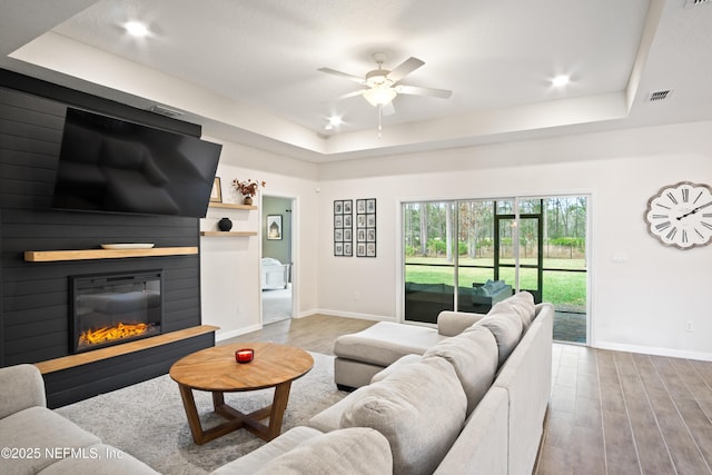 living room with a tray ceiling, ceiling fan, and light hardwood / wood-style flooring