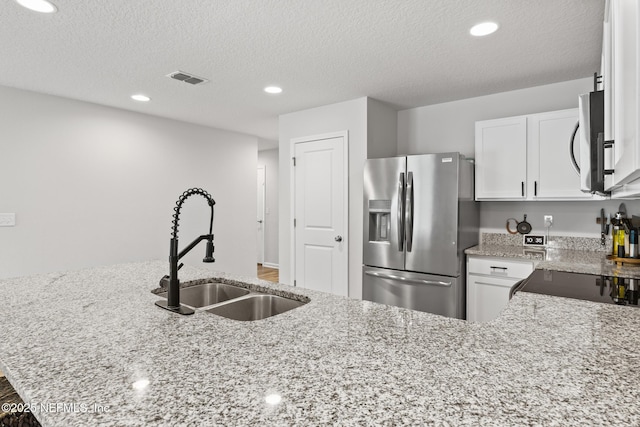 kitchen with visible vents, a sink, white cabinetry, light stone countertops, and stainless steel appliances