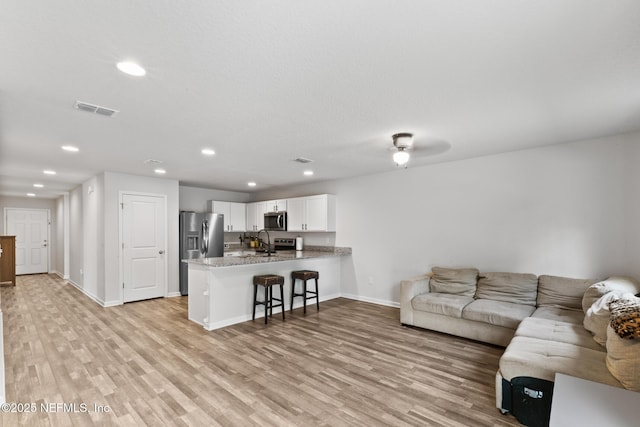 living room with visible vents, baseboards, recessed lighting, and light wood-style floors
