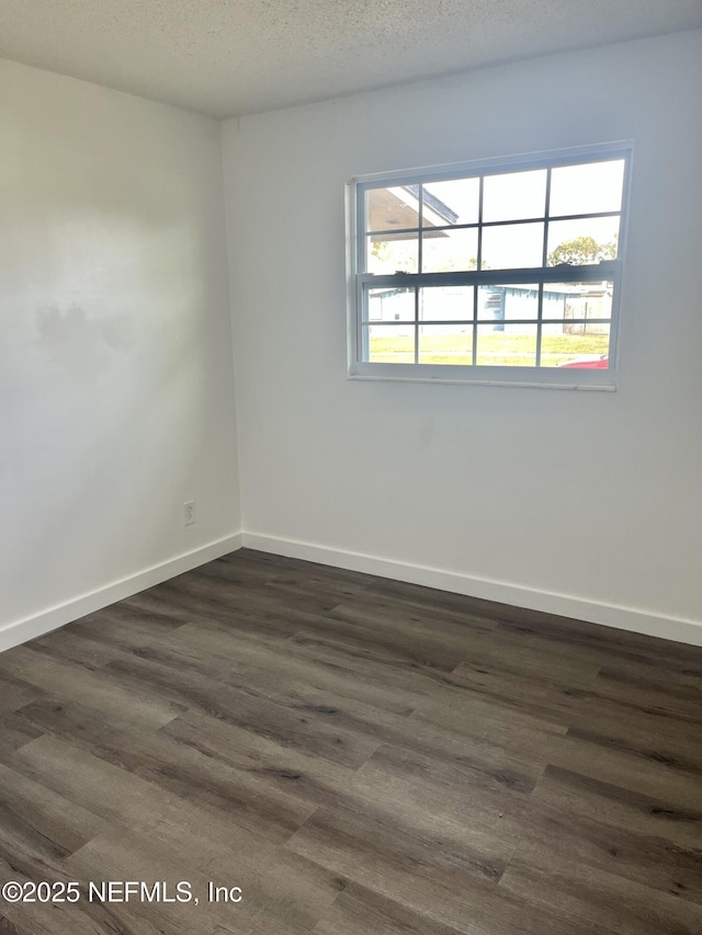 empty room featuring a textured ceiling, dark wood-type flooring, and baseboards