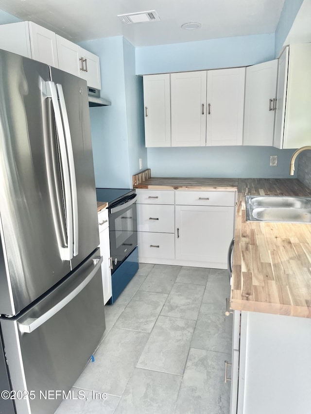 kitchen featuring butcher block counters, electric range, freestanding refrigerator, and a sink