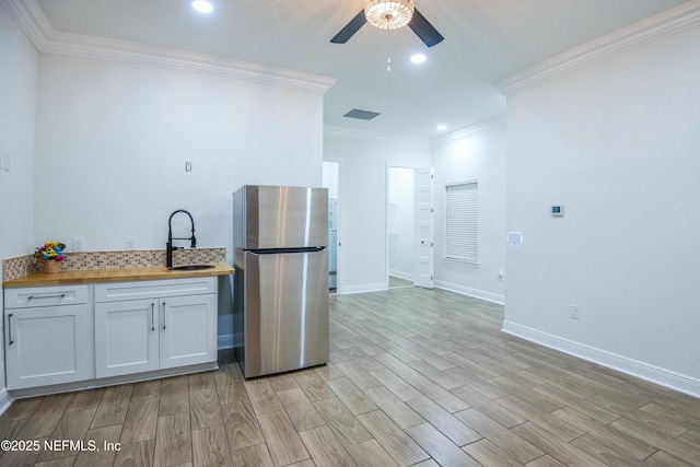 kitchen featuring butcher block countertops, crown molding, stainless steel fridge, sink, and white cabinetry