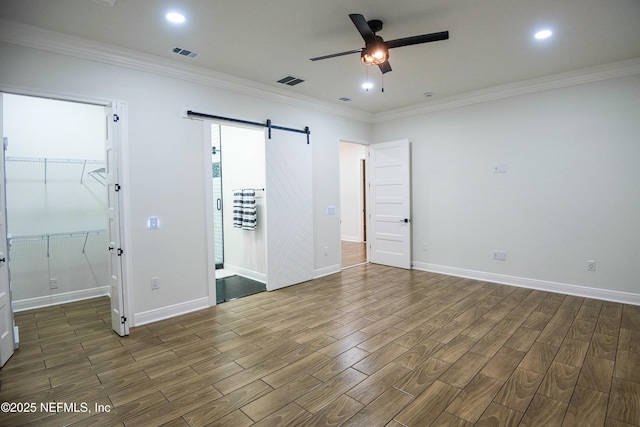 unfurnished bedroom with ornamental molding, a barn door, and ceiling fan