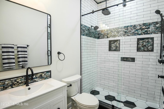 bathroom with toilet, tiled shower, and vanity