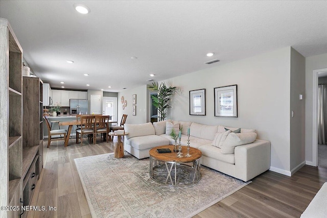 living area with recessed lighting, visible vents, baseboards, and light wood finished floors