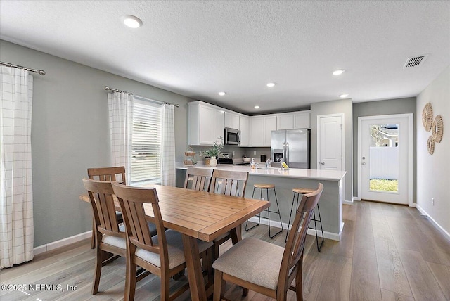 dining space featuring visible vents, a textured ceiling, light wood-type flooring, and baseboards