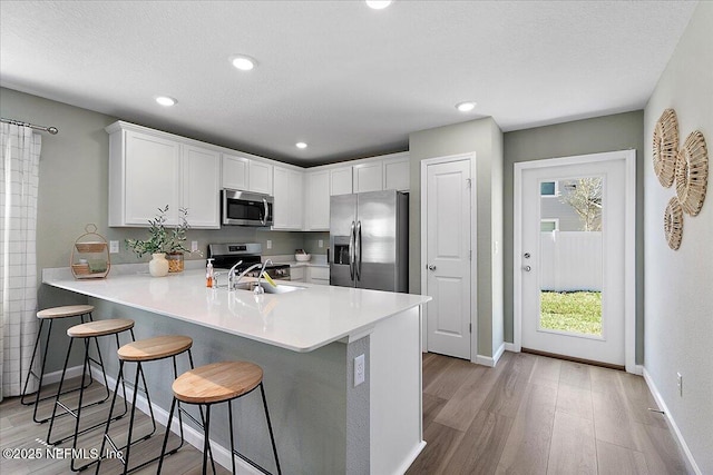 kitchen featuring a sink, stainless steel appliances, a peninsula, a breakfast bar area, and light wood finished floors