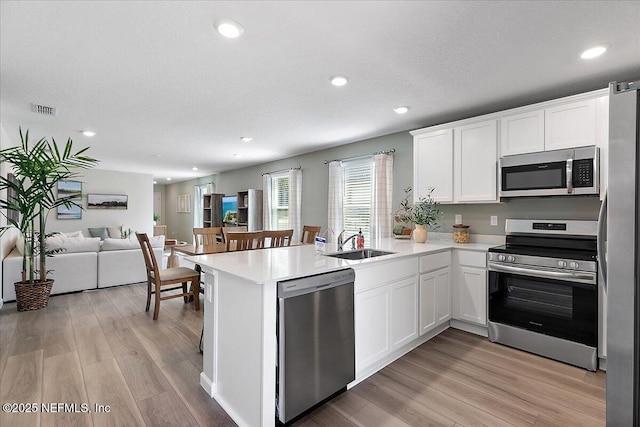 kitchen featuring visible vents, a sink, open floor plan, stainless steel appliances, and a peninsula