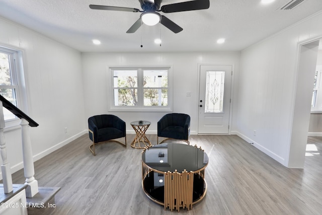 living area featuring baseboards, light wood-style flooring, visible vents, and a textured ceiling