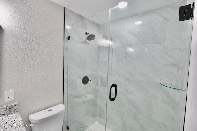 full bathroom featuring a textured wall, vanity, a shower stall, and toilet