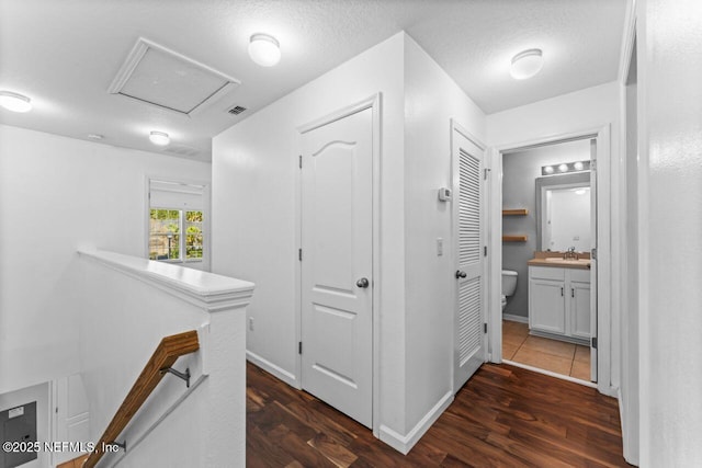 corridor with dark wood-style floors, a sink, an upstairs landing, and attic access