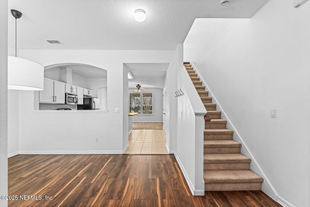 foyer featuring ceiling fan, stairs, visible vents, and dark wood-type flooring