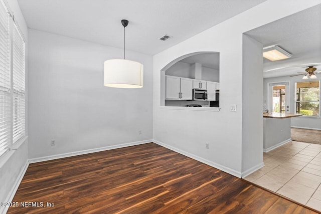 unfurnished dining area with a ceiling fan, visible vents, baseboards, and wood finished floors