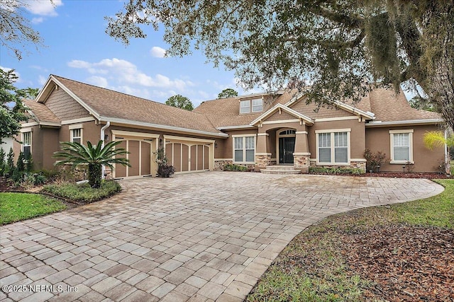 craftsman house featuring stone siding, decorative driveway, an attached garage, and stucco siding