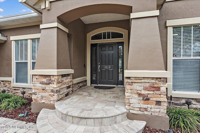 doorway to property featuring stone siding and stucco siding