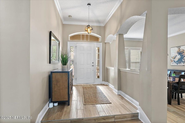 entryway with baseboards, arched walkways, a textured ceiling, crown molding, and light wood-style floors