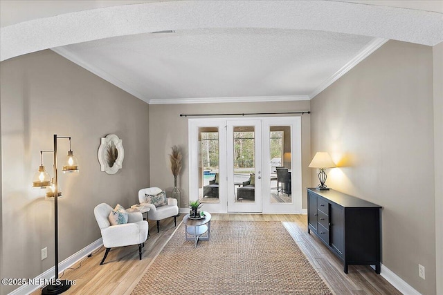 sitting room with ornamental molding, baseboards, a textured ceiling, and light wood finished floors