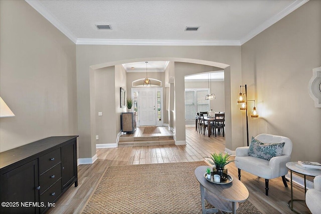 entryway featuring arched walkways, ornamental molding, visible vents, and light wood-style floors