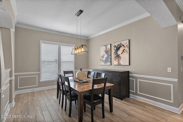 dining room with crown molding, light wood-style flooring, and a decorative wall