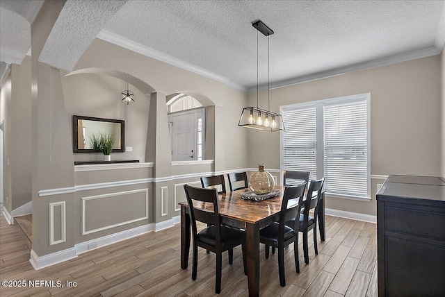 dining room with light wood-style floors, ornamental molding, a textured ceiling, and baseboards