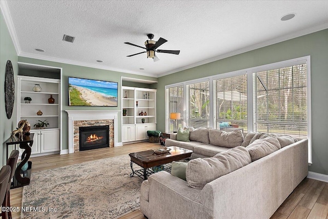 living area featuring light wood-type flooring, ornamental molding, a textured ceiling, and a glass covered fireplace